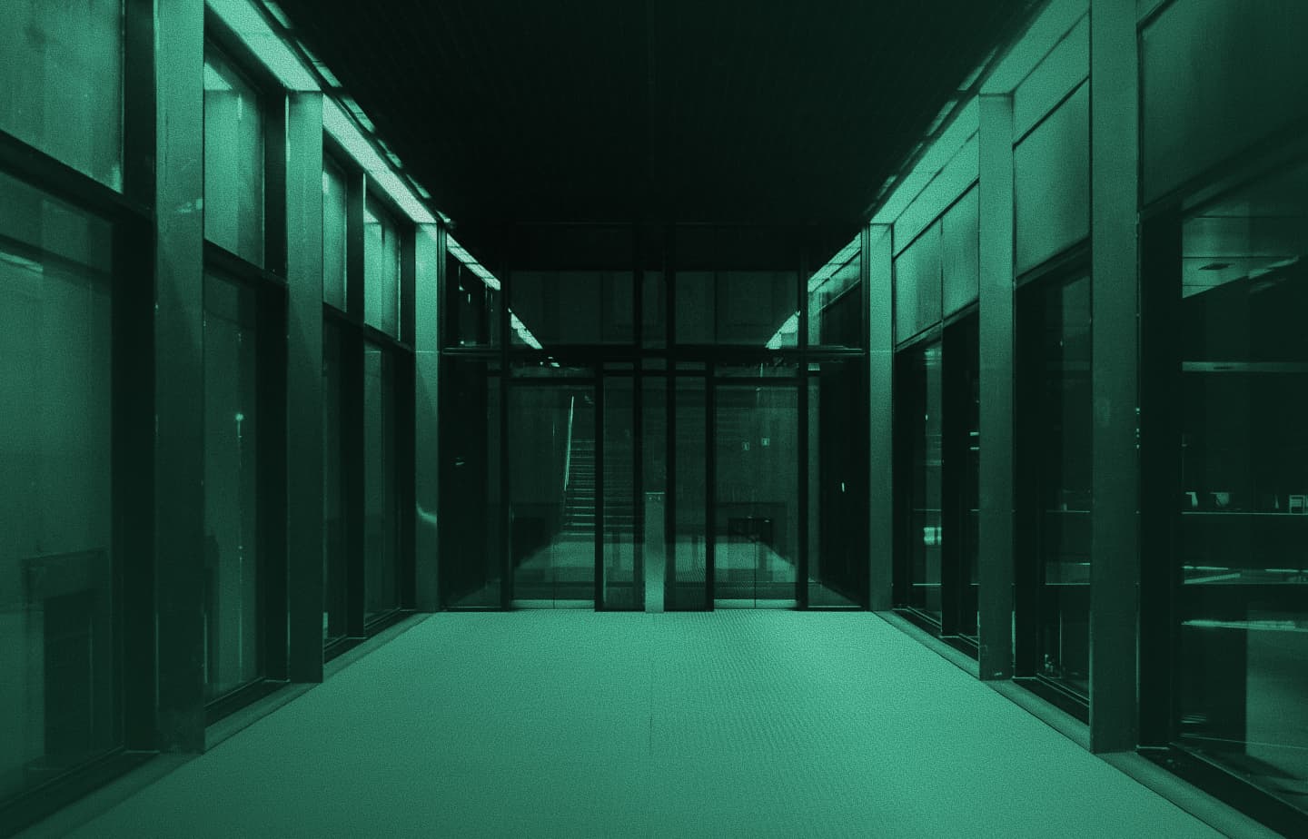 Long glass-walled office corridor leading to a staircase, teal monochrome photo