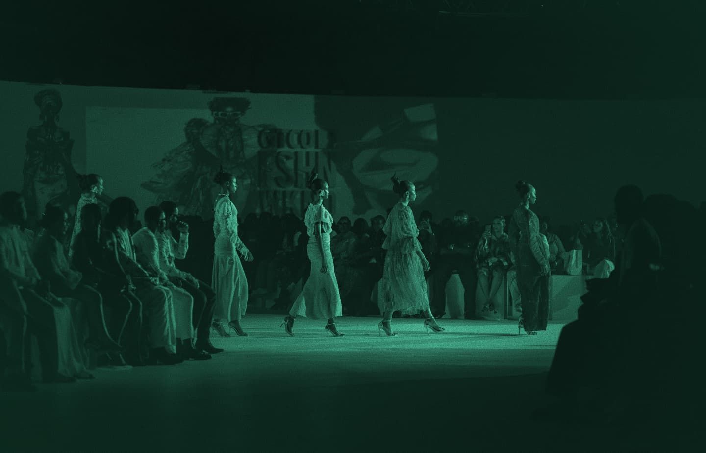 Models walking a fashion runway before an audience, green-tinted photo