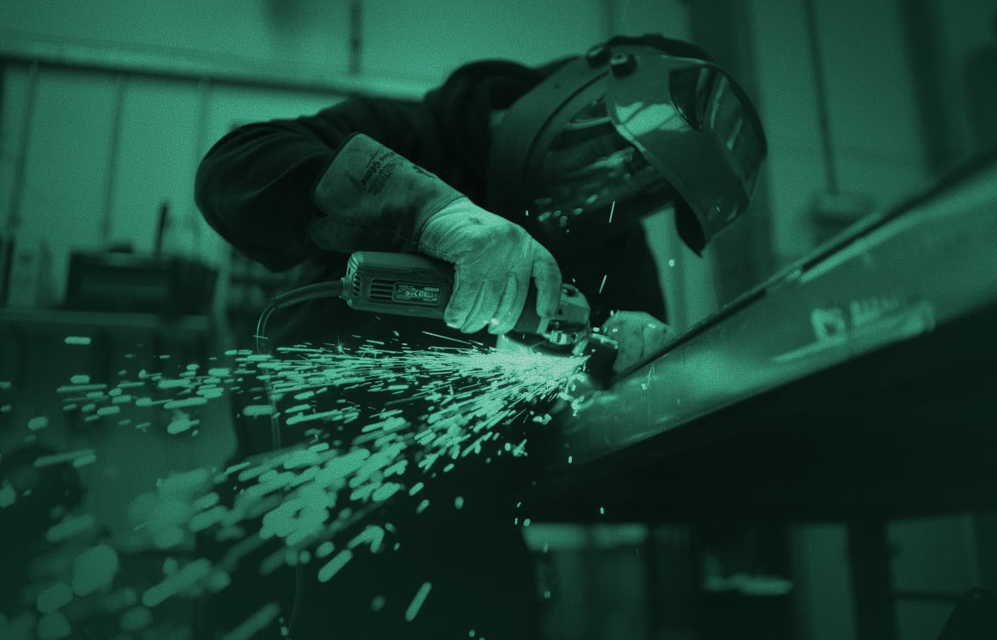 Welder in protective gear grinding metal with sparks flying in a workshop, green tint