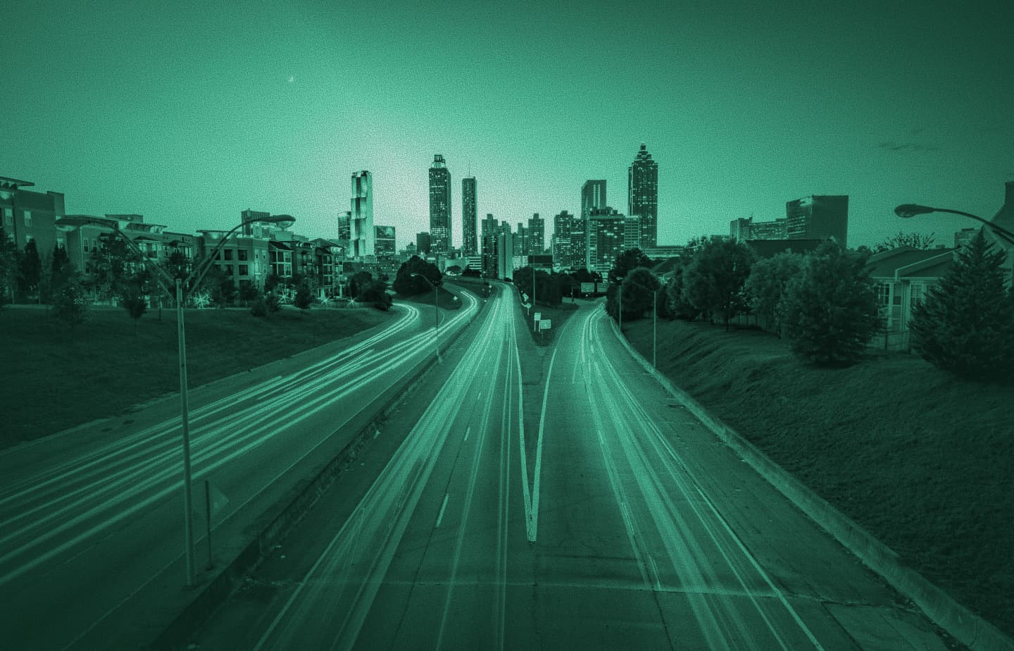Night city skyline with long-exposure traffic light trails on a highway, teal tint