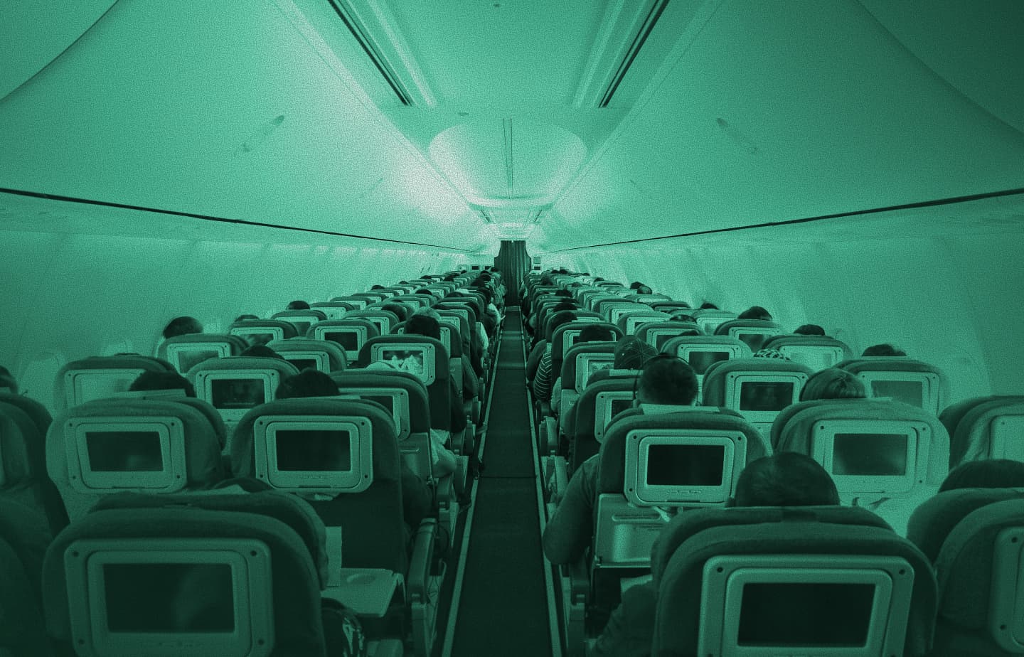 Interior of a passenger aircraft cabin looking down the centre aisle, green tint