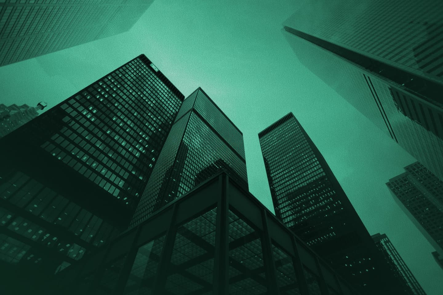 Low-angle view looking up at glass office skyscrapers with a green monochrome tint