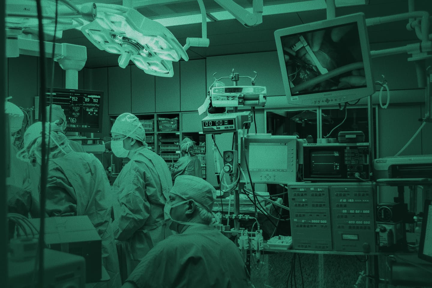 Surgical team in an operating theatre with monitors and equipment, green-tinted photo