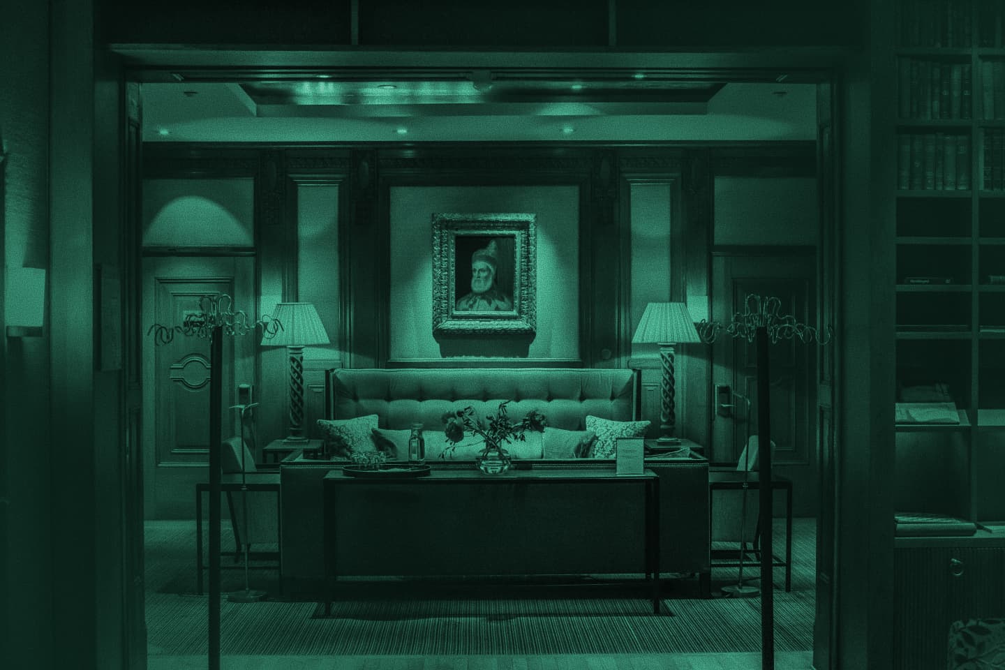 Green-tinted photo of a formal hotel suite with a tufted headboard, lamps and a framed portrait